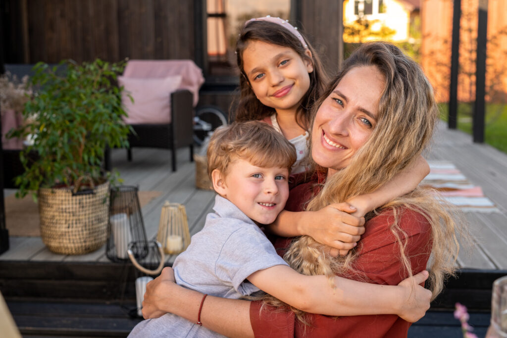 A mother in recovery sitting outside with her two children, all smiling together, symbolizing resilience in overcoming challenges.