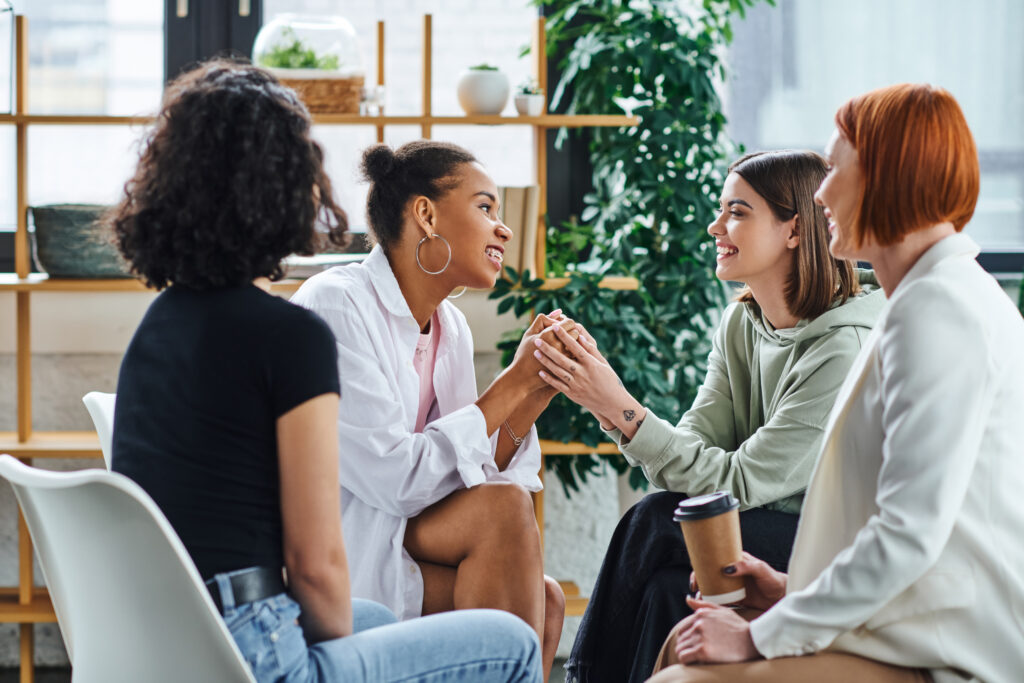 A group of supportive women gathered in a circle, offering encouragement to a mother in recovery as they hold hands.